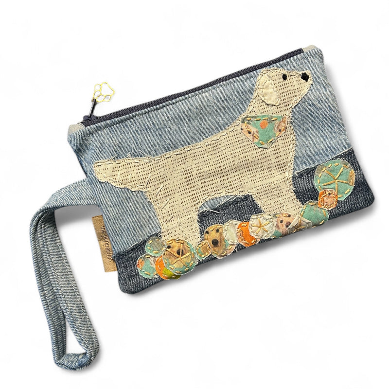 The Pupperfish Handmade and hand embroidered zipper pouch with upcycled denims and fabrics, featuring a golden retriever playing near the water with beach balls at its feet. 